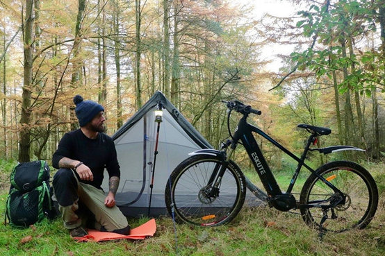 En elcykel står bredvid en man som campar djupt i skogen