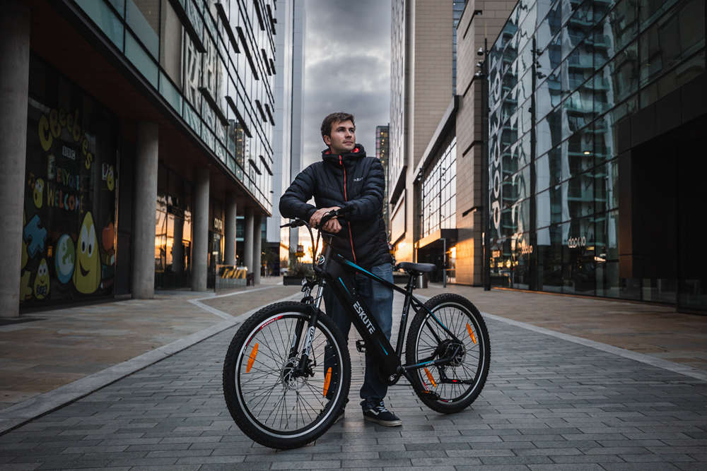 En man står på gatan och håller sin pendlar-elcykel