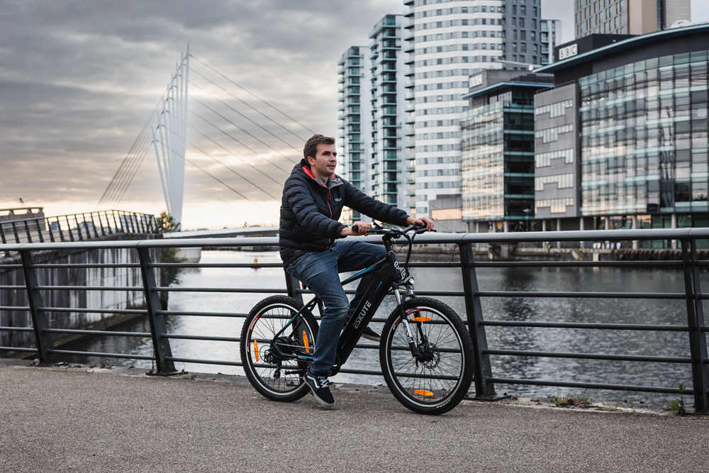 En man cyklar med sin elcykel längs floden i staden