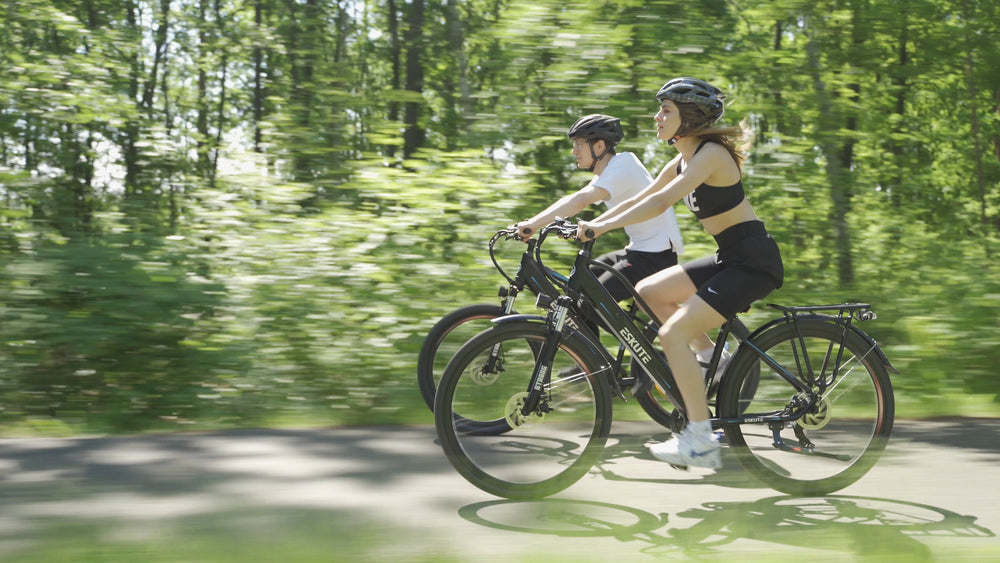 En man och en kvinna med MTB-hjälmar cyklar på elcyklar på en skuggig stig