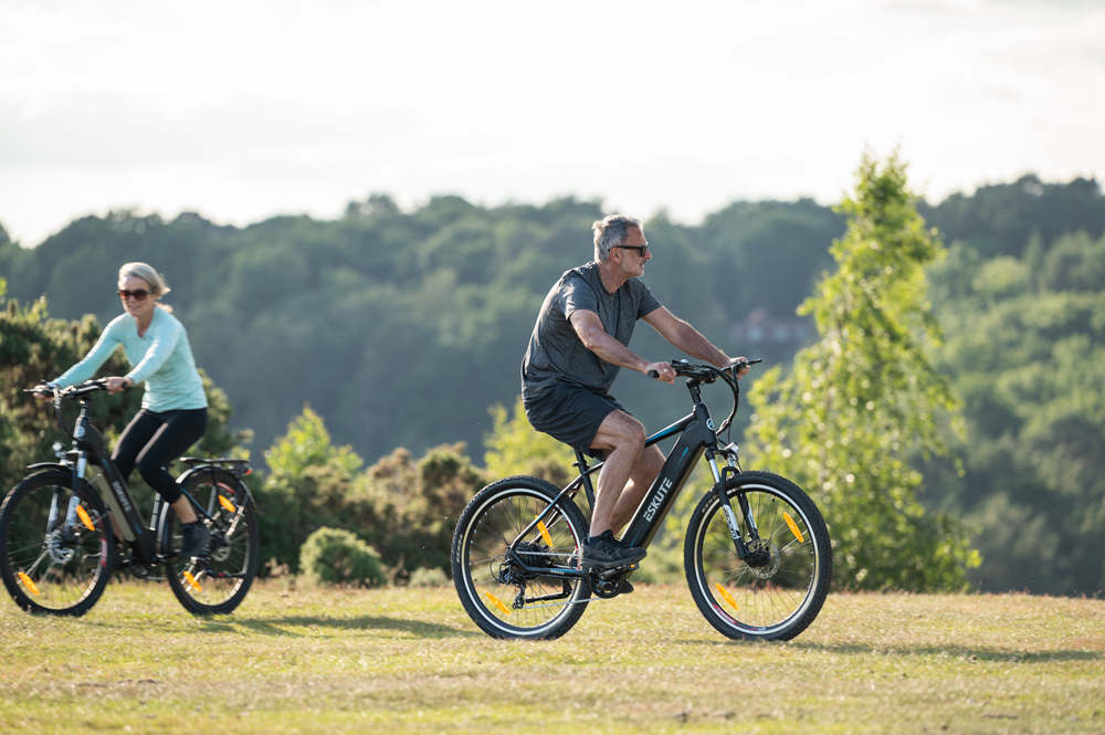 En man och en kvinna cyklar med sina elcyklar över ängen