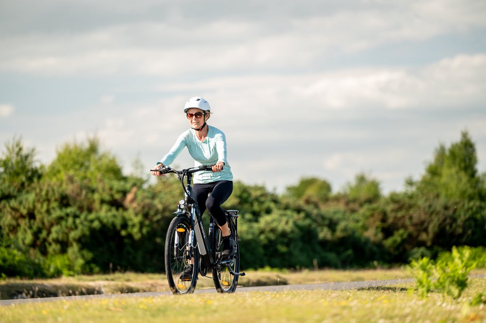 En dam med enkel MTB-hjälm cyklar med elcykel på ängen