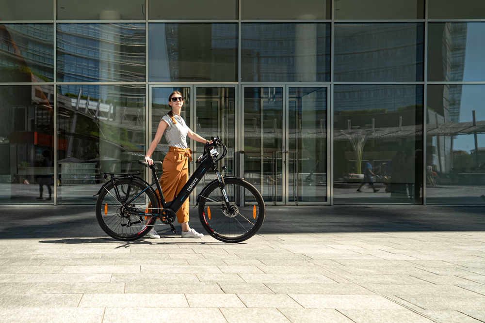 En kvinna står med sin elcykel framför en byggnad