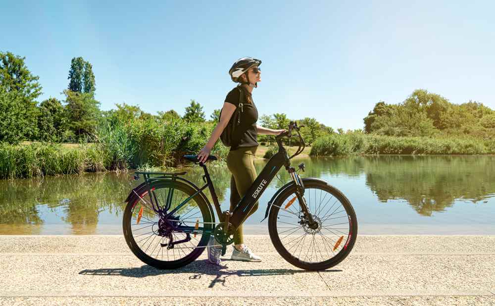 En kvinna med hjälm som cyklar på en elektrisk vandringscykel står nära en sjö