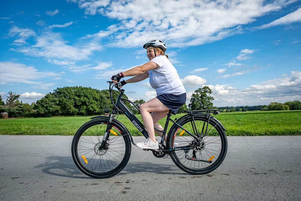 En kvinna med hjälm cyklar på sin elektriska sparkcykel på vägen