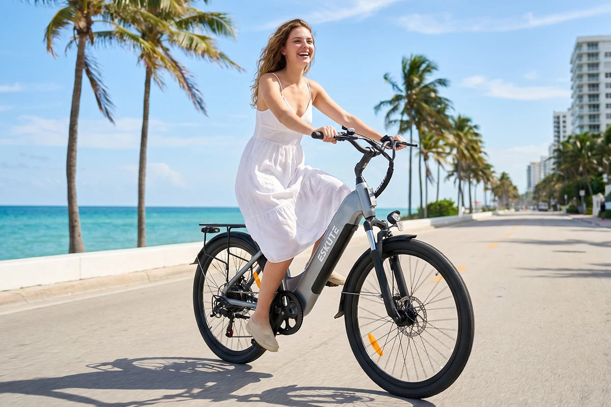 Frau fährt das graue C202 City-E-Bike entlang einer sonnigen Küstenpromenade mit Meer und Palmen