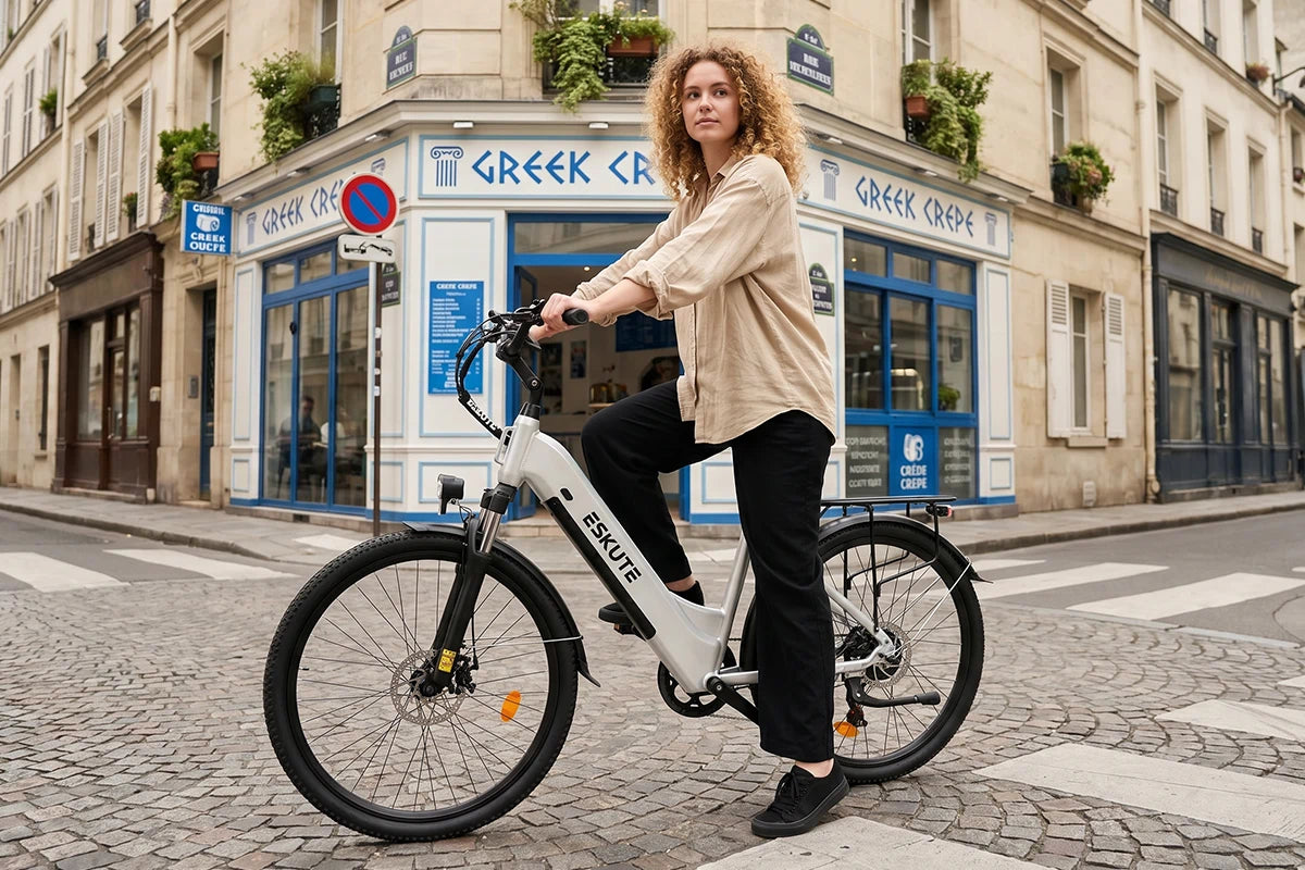 En kvinna cyklar på en vit C202 stadse-bike genom en franskinspirerad gata med ett klassiskt café.