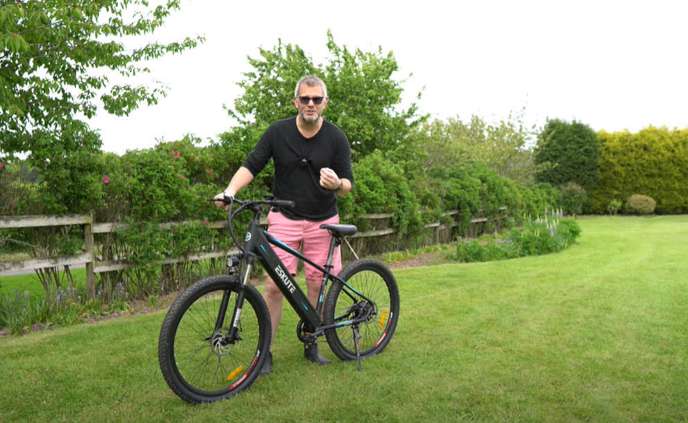 ein-mann-mit-brille-stellt-sein-e-bike-auf-der-wiese-vor-dem-mountainbiken-vor