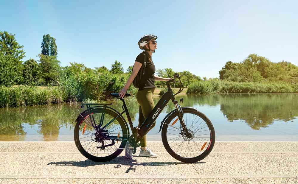 en kvinna med hjälm som står vid sjön med sina elektriska trekkingcyklar