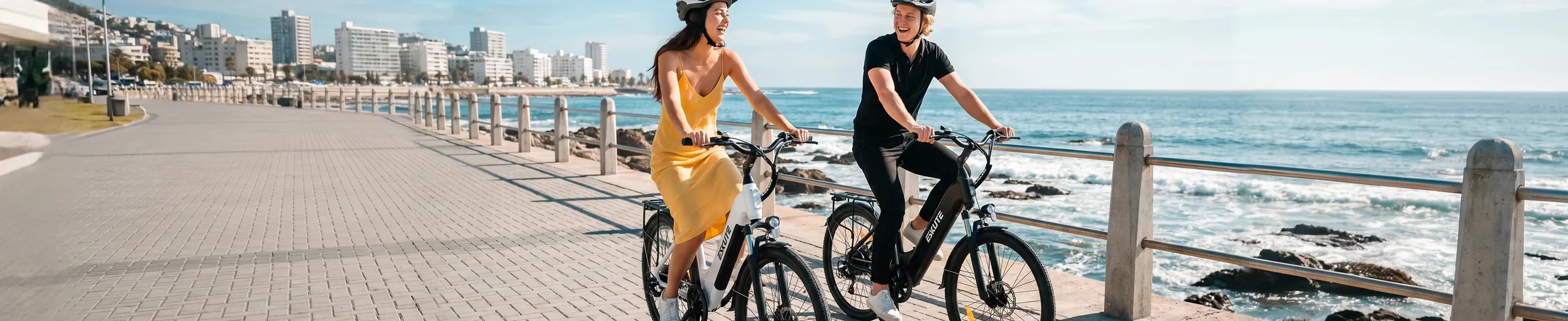 Paar fährt Eskute E-Bikes entlang eines Küstenparks in entspannter Atmosphäre