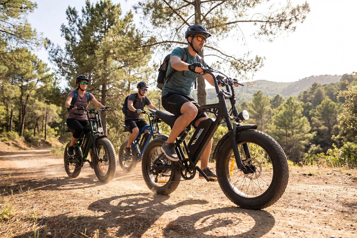 A group of cyclists riding V202 all-terrain fat tire electric bicycles through a sunny forest dirt trail.
