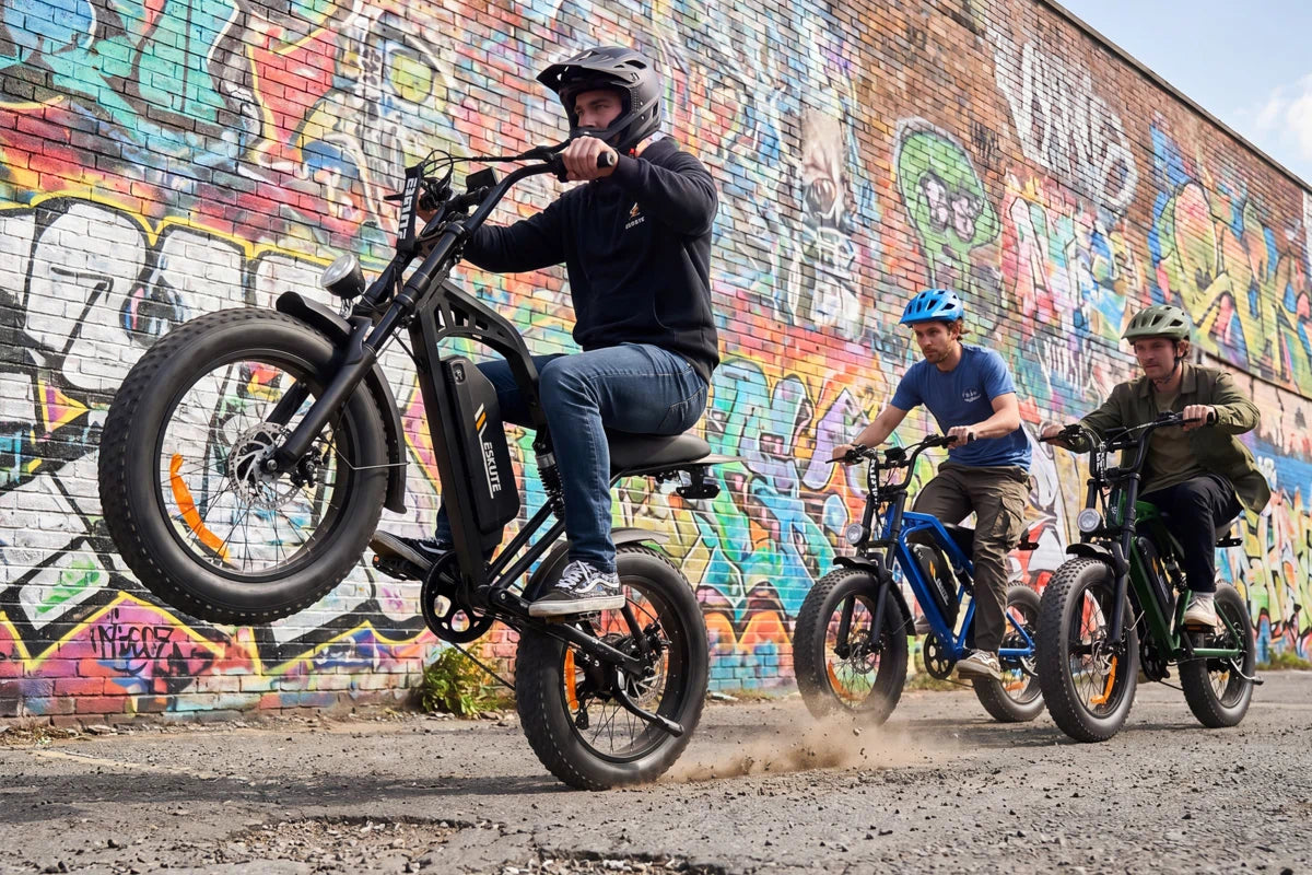 A rider performing a wheelie stunt on a black V202 fat tire ebike in front of a colorful graffiti wall in the city.