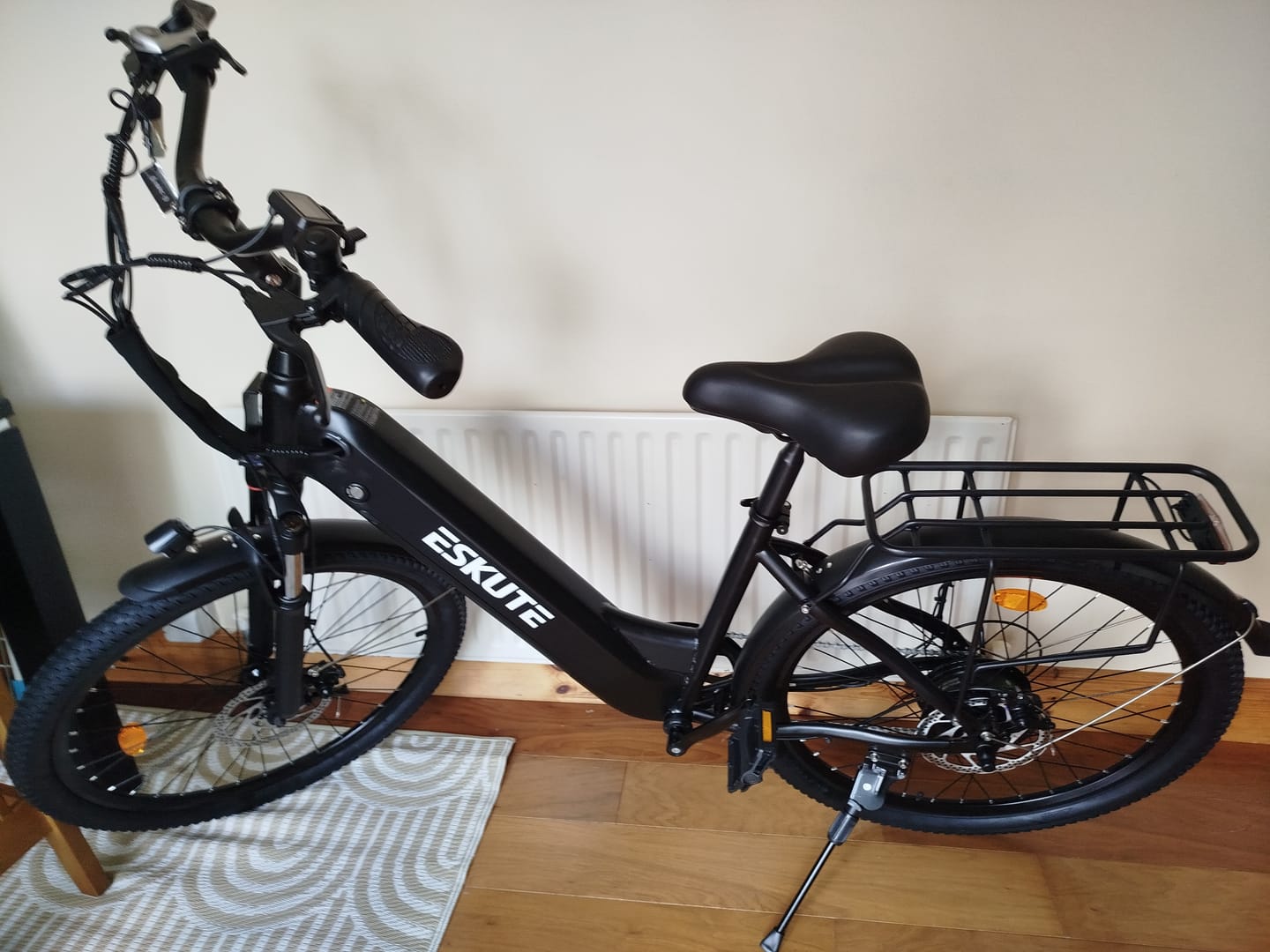 Customer's black Eskute C202 City E-Bike parked indoors on a rug with a kickstand deployed.
