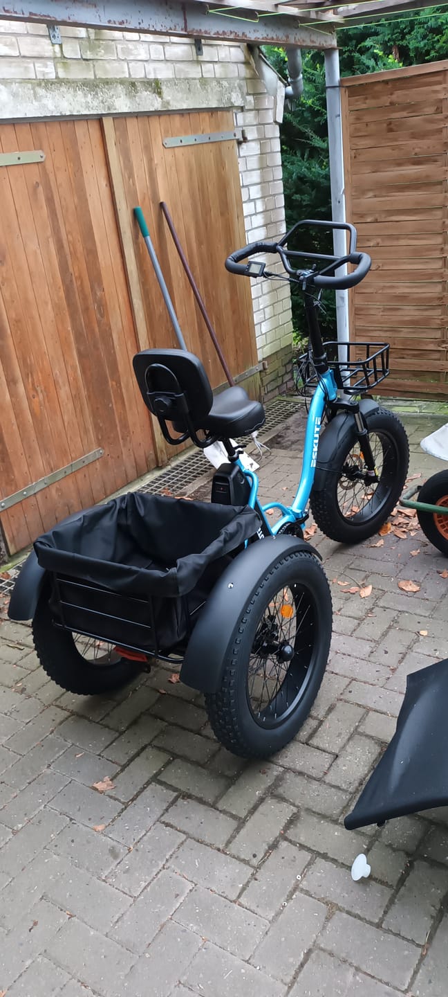 Customer's blue three-wheeled bike with a rear storage basket and padded seat, parked outdoors on a paved patio.