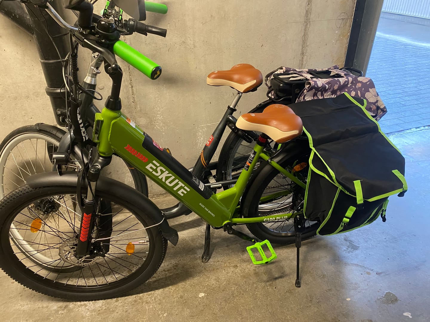 Customer's green Eskute C100 Plus City E-Bike with a large black storage bag parked indoors.