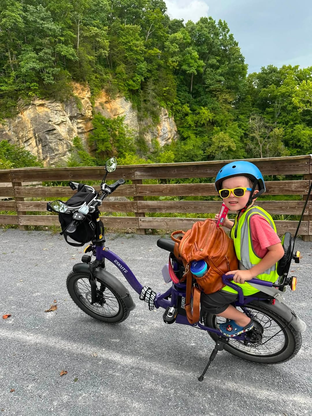 Customer's purple Eskute D202 Folding-E-Bike on a gravel path with a child wearing a helmet and vest on the back