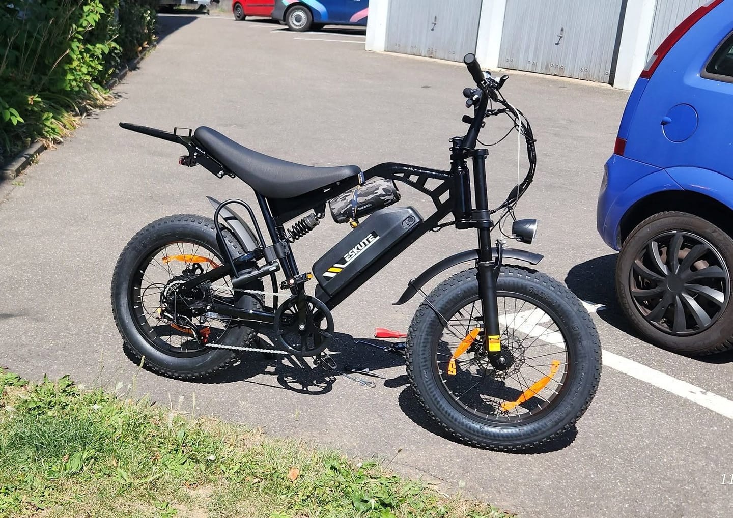 Reviewer's black Eskute V202 retro e-bike parked on an asphalt lot beside a blue car