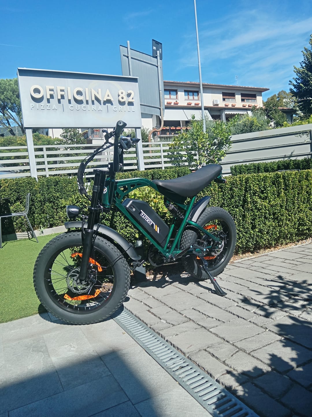 Customer's green Eskute V202 e-bike parked on a paved walkway outside a building.
