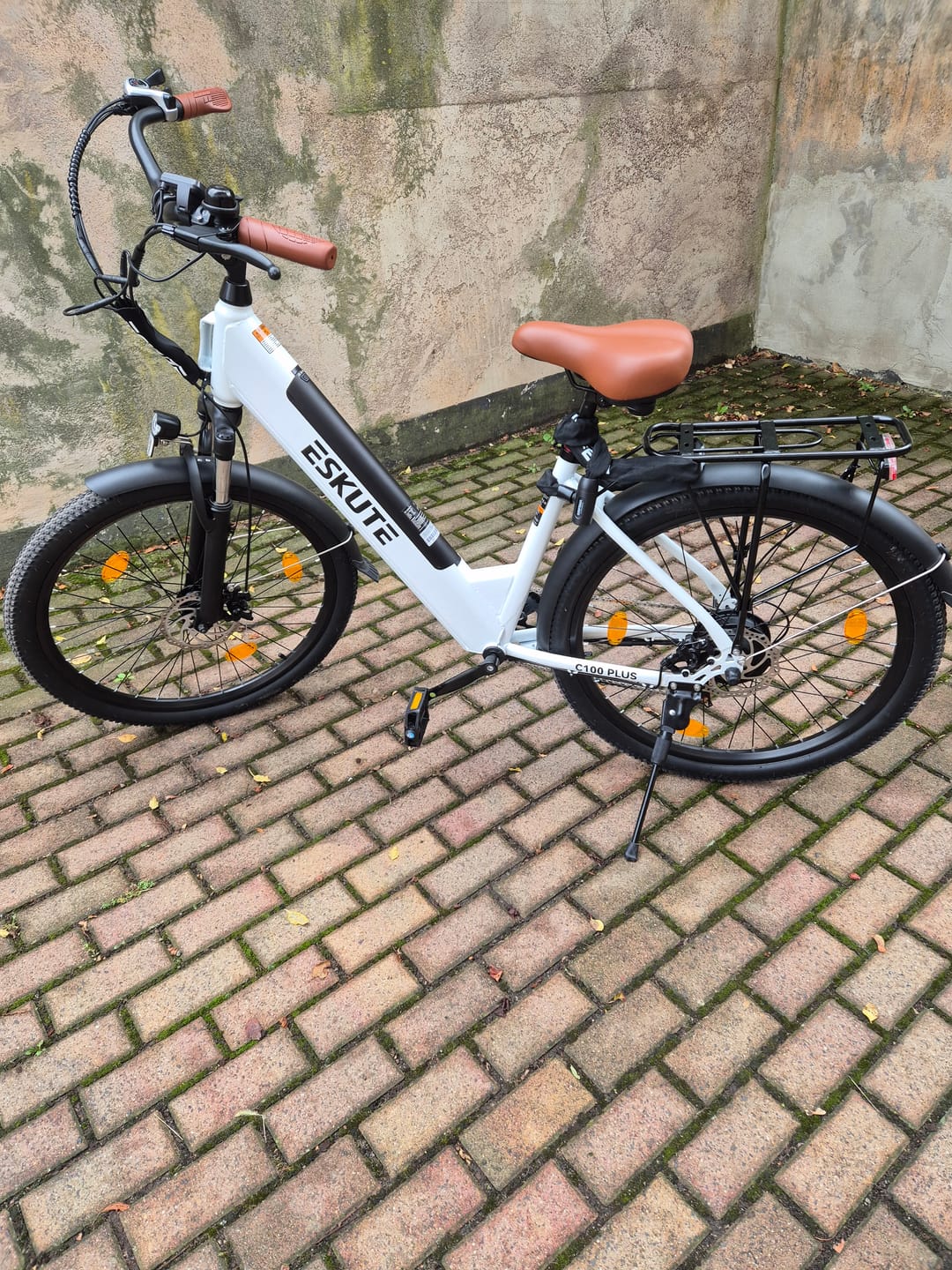 Customer's white Eskute C100 Plus City E-Bike parked on a paved stone ground, showing the frame, seat, and handlebars.