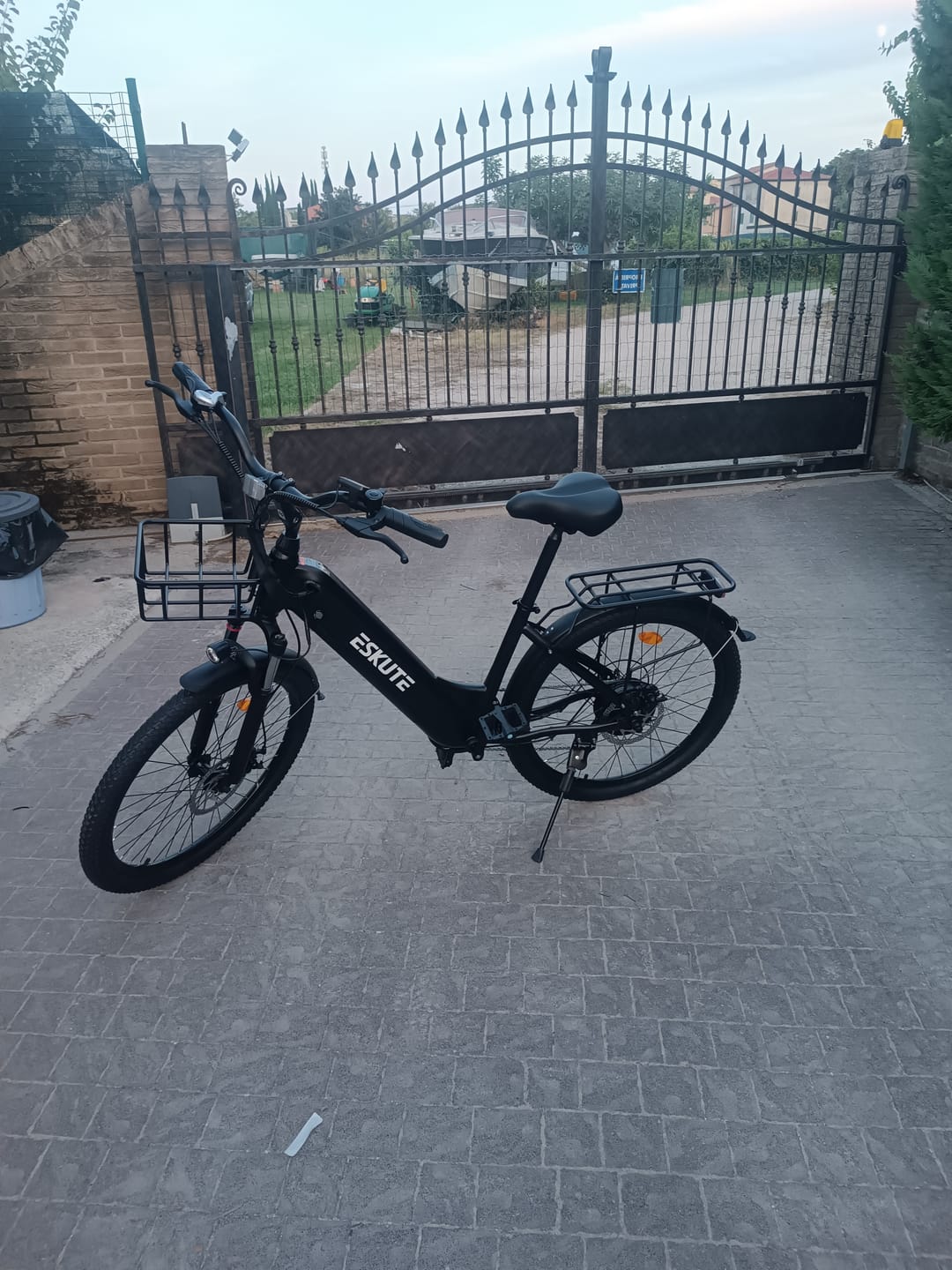 Customer's black Eskute C202 City E-Bike parked on a paved driveway with a metal gate in the background.