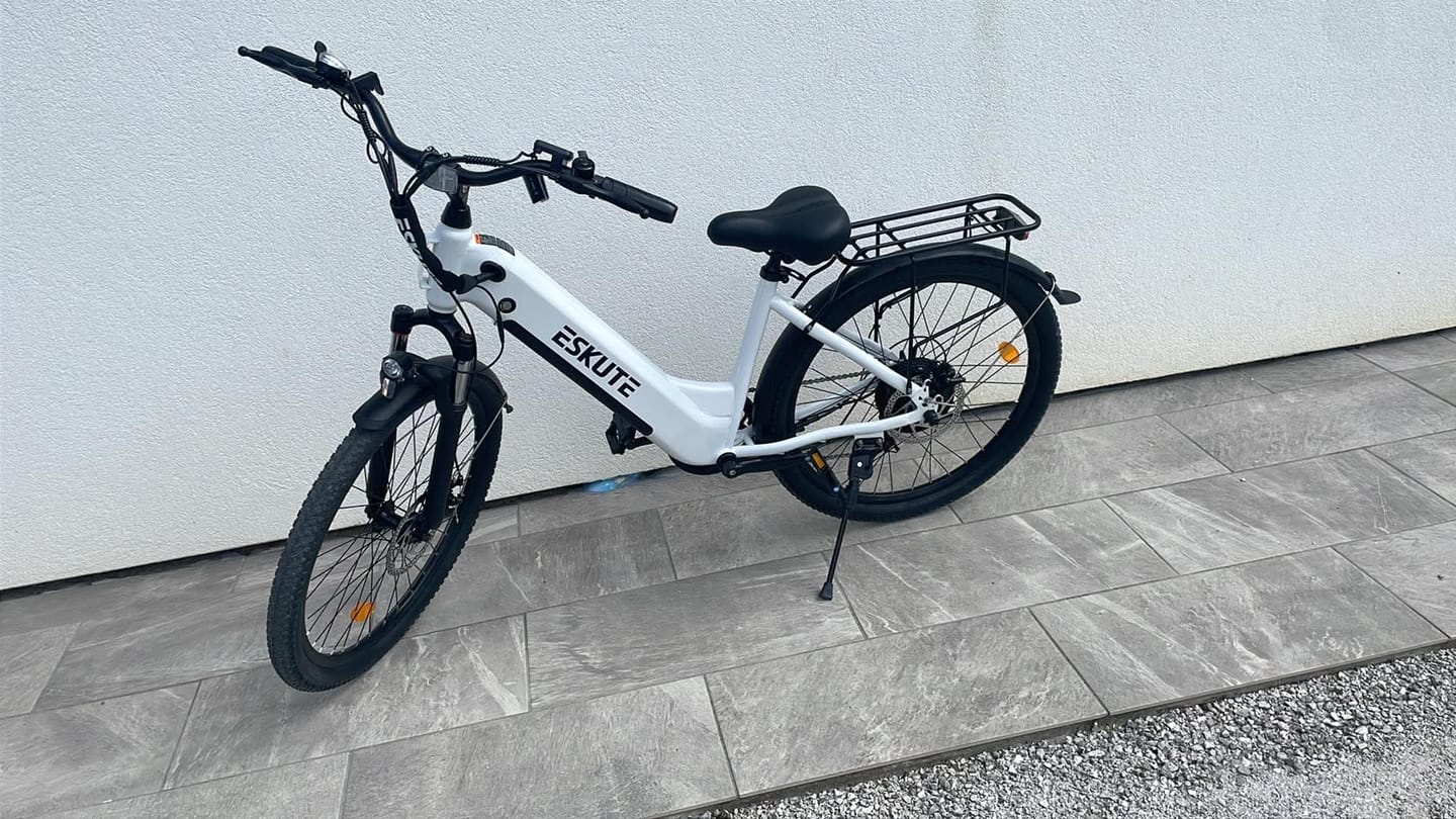 Customer's white Eskute C202 City E-Bike parked on tiled ground against a white wall